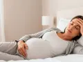 Zmęczona ciężarna odpoczywa w łóżku, czując senność w ciąży. Dłoń na czole, oczy zamknięte.
