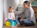 Mama uczy dziecko, jak nauczyć dziecko korzystać z nocnika. Maluch siedzi na kolorowym nocniku, mama siedzi obok.