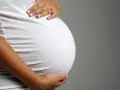 Brzuch ciężarnej kobiety w białej bluzce, dłonie delikatnie go obejmują. Zbliża się poród, może już wkrótce pojawi się czop śluzowy.