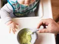 Maluch w śliniaczku dostaje łyżeczkę z puree z awokado dla niemowlaka.