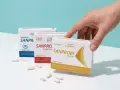 Dłoń sięga po probiotyk w ciąży. Na stole leżą opakowania Sanprobi, a obok nich kapsułki.