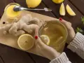 Ciepła herbata z imbirem i cytryną, idealna na mdłości w ciąży. Na desce leżą świeży imbir, cytryna i miód.