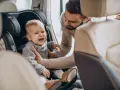 Płaczące dziecko w foteliku samochodowym. Tata próbuje je uspokoić. Zastanawiasz się, do kiedy fotelik dla dziecka jest potrzebny?
