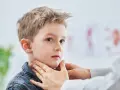 Lekarz bada szyję chłopca, sprawdzając, czy nie ma powiększonych węzłów chłonnych u dzieci. Zdjęcia takie pokazują ważny element diagnostyki.