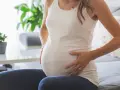 Kobieta w ciąży siedzi na kanapie, dotykając brzucha. Zauważyła brązowe plamienie w ciąży, co ją martwi.