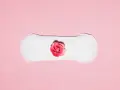 Biały podpaska z różową różą pośrodku. Symbolizuje cykl menstruacyjny, gdzie skrzep czy zarodek może być częścią tej naturalnej podróży.