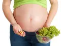 Kobieta w ciąży trzyma garść tabletek i miskę sałatki. Ważne jest żelazo dla kobiet w ciąży, czy wybrać suplementy czy zdrową dietę?