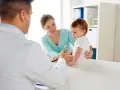 Pediatra bada niemowlę podczas pierwszej wizyty. Mama z uśmiechem obserwuje badanie.
