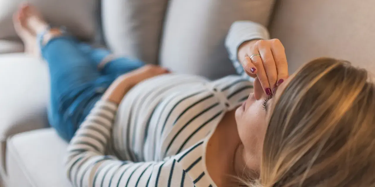 Kobieta w ciąży leży na kanapie, dotykając czoła. Zmartwienie o brak bicia serca w 8 tygodniu ciąży maluje się na jej twarzy.