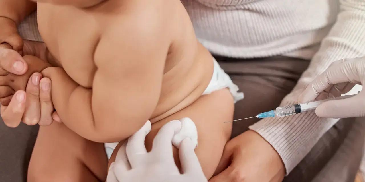 Dziecko otrzymuje szczepienie. Ręka w rękawiczce trzyma strzykawkę, a druga ręka przygotowuje miejsce wkłucia. To ważny moment dla zdrowia, jak w przypadku szczepionki heine medina.