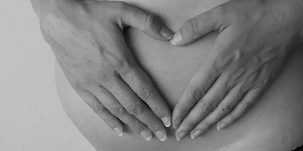 Dłonie tworzą serce na brzuchu ciężarnej. Intensywne ruchy dziecka mogą być sygnałem niedotlenienia.