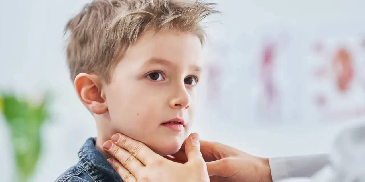 Lekarz bada szyję chłopca, sprawdzając, czy nie ma powiększonych węzłów chłonnych u dzieci. Zdjęcia takie pokazują ważny element diagnostyki.