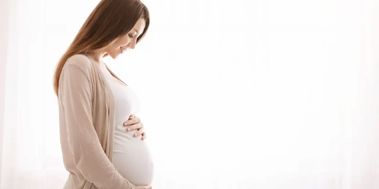 Kobieta w ciąży z hashimoto delikatnie dotyka brzucha, patrząc na niego z miłością.