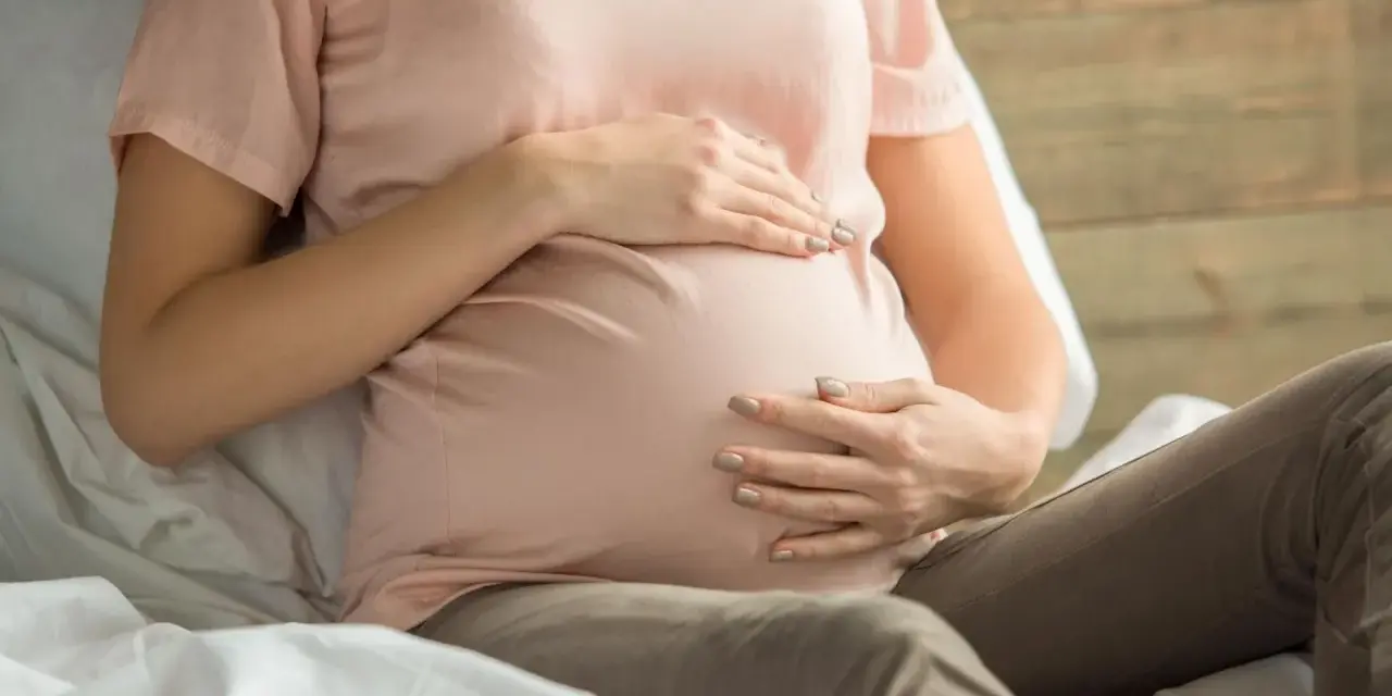 Kobieta w ciąży z dłońmi na brzuchu, martwiąca się o niskie erytrocyty w ciąży.