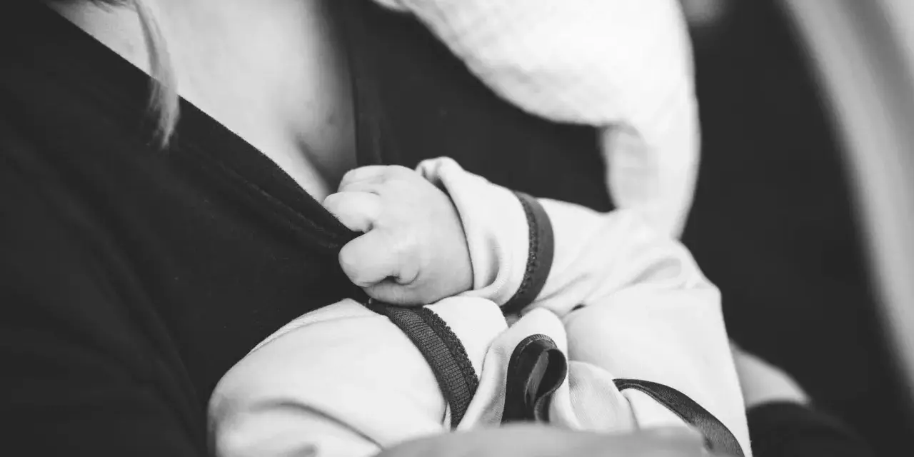 Dłoń noworodka chwyta ubranie mamy. Delikatne paluszki, które mogą wywołać **baby blues**, ale też ogromną miłość.