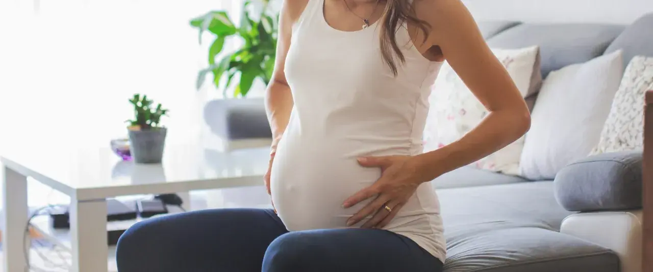 Kobieta w ciąży siedzi na kanapie, dotykając brzucha. Zauważyła brązowe plamienie w ciąży, co ją martwi.