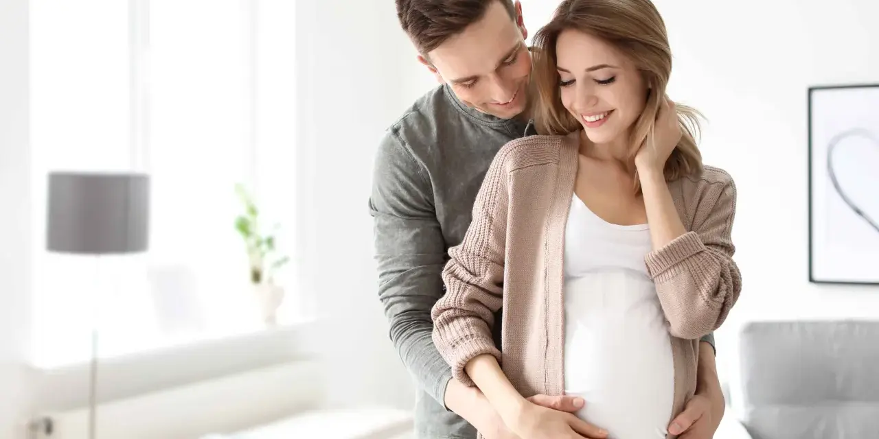 Szczęśliwy mąż obejmuje żonę w ciąży, okazując troskę i miłość. To piękny obraz wsparcia i oczekiwania na dziecko, symbolizujący opiekę na żonę po porodzie.