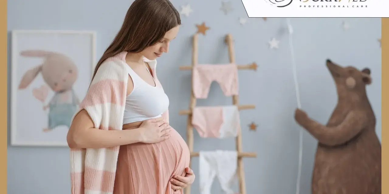 Jestem w ciąży, w 32 tygodniu. Delikatnie dotykam brzucha w pokoju dziecięcym z pluszowym misiem i ubrankami.