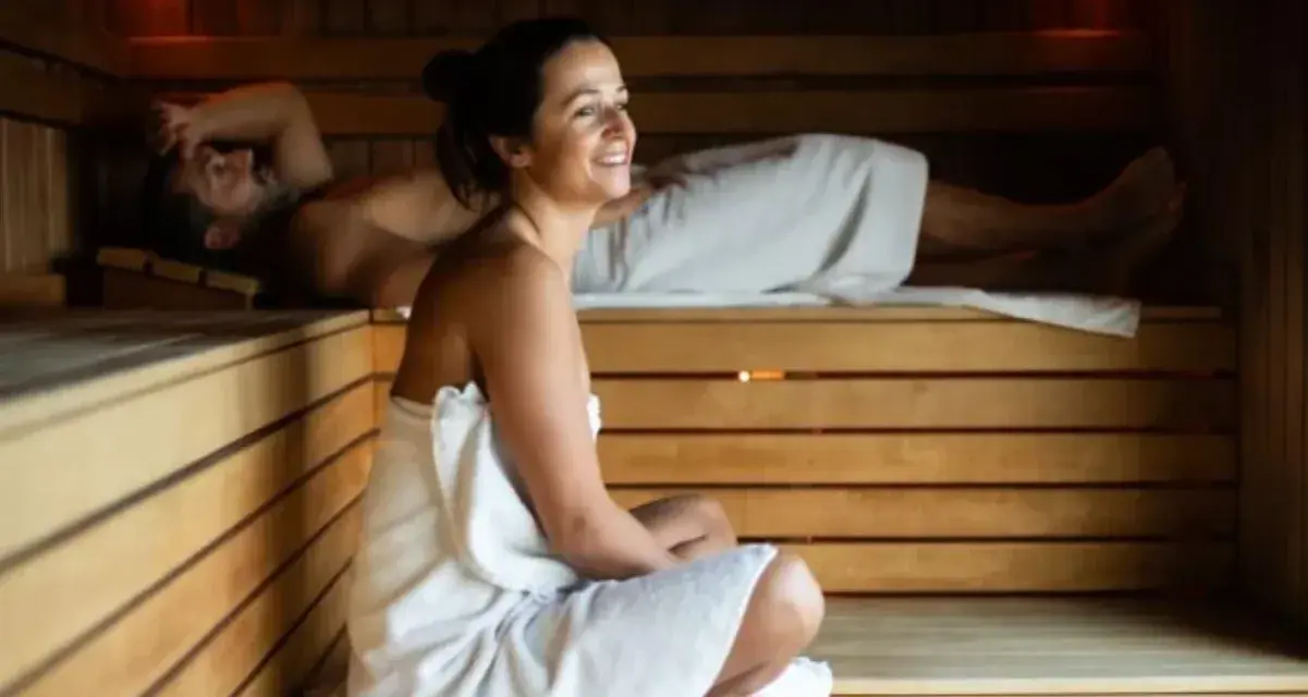 Para relaksu w saunie. Kobieta w ciąży i mężczyzna odpoczywają w drewnianej saunie, otuleni ręcznikami.