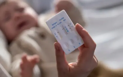 Dłoń trzyma test combo na COVID-19, grypę i RSV. W tle niewyraźne dziecko.