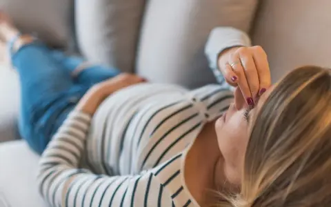Kobieta w ciąży leży na kanapie, dotykając czoła. Zmartwienie o brak bicia serca w 8 tygodniu ciąży maluje się na jej twarzy.