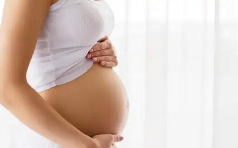 Brzuch kobiety w ciąży, delikatnie dotykany dłońmi. Temat: grzybica pochwy w ciąży.