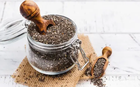 Słoik pełen nasion chia, idealnych dla kobiet w ciąży, z drewnianą łyżką. Nasiona chia to bogactwo kwasów omega-3 i błonnika.
