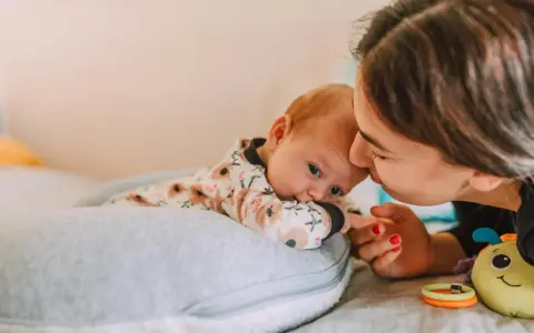 Mama pochyla się nad dzieckiem, które leży na poduszce. Szybki oddech u noworodka może być naturalny, ale czujność rodzica jest ważna.