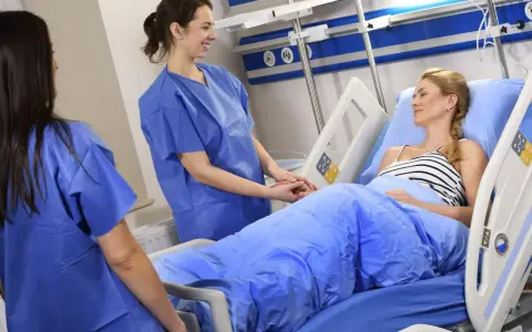 Dwie pielęgniarki w niebieskich fartuchach troskliwie opiekują się pacjentką w łóżku szpitalnym. Czy to CMV?