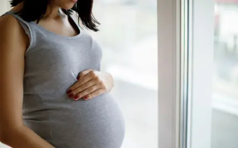 Kobieta w ciąży, która czeka na poród, delikatnie dotyka brzucha. Może to być związane z ćwiczeniami na wywołanie porodu.
