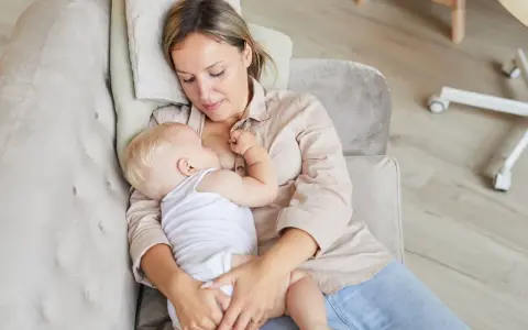 Mama karmi dziecko spod pachy na kanapie. Ciepła chwila bliskości i spokoju.
