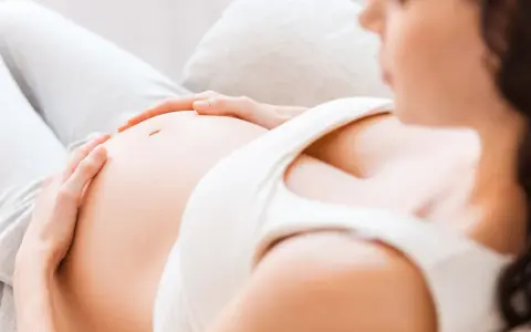 Kobieta w 7 miesiącu ciąży delikatnie głaszcze swój brzuszek.