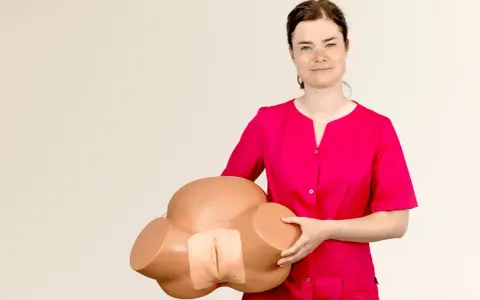 Kobieta w różowej bluzce prezentuje model miednicy do nauki masażu krocza przed porodem.