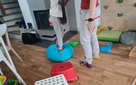 Dziecko ćwiczy równowagę na niebieskiej poduszce, część domowej ścieżki sensorycznej dla dzieci.