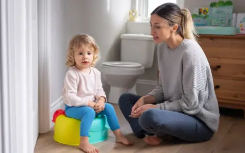 Mama uczy dziecko, jak nauczyć dziecko korzystać z nocnika. Maluch siedzi na kolorowym nocniku, mama siedzi obok.