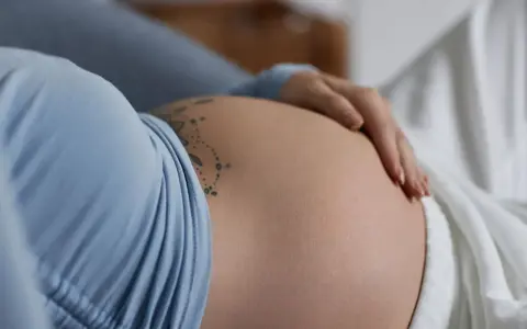 Dłoń delikatnie głaszcze ciążowy, twardy brzuch z tatuażem.