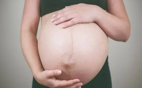 Dłońmi obejmuje zaokrąglony brzuch, czując delikatne ruchy dziecka w brzuchu.