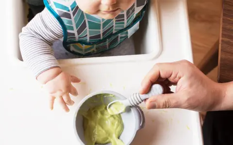 Maluch w śliniaczku dostaje łyżeczkę z puree z awokado dla niemowlaka.