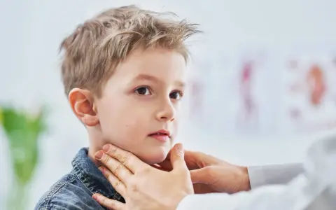 Lekarz bada szyję chłopca, sprawdzając, czy nie ma powiększonych węzłów chłonnych u dzieci. Zdjęcia takie pokazują ważny element diagnostyki.