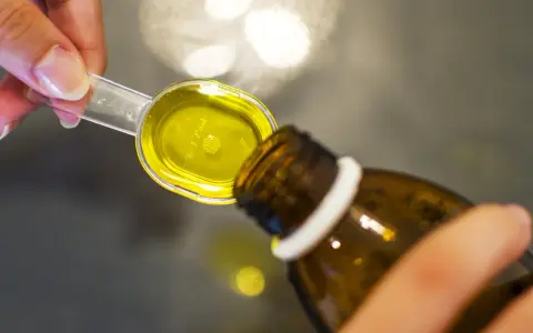 Kobieta odmierza syrop prawoślazowy w ciąży. Płynna, żółta substancja wypełnia miarkę.