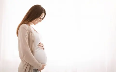 Kobieta w ciąży z hashimoto delikatnie dotyka brzucha, patrząc na niego z miłością.
