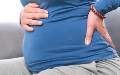 Kobieta w ciąży trzyma się za brzuch i plecy, odczuwając dyskomfort. To może być objaw biegunki przed porodem.