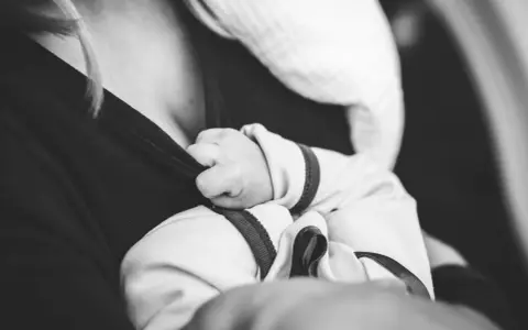 Dłoń noworodka chwyta ubranie mamy. Delikatne paluszki, które mogą wywołać **baby blues**, ale też ogromną miłość.