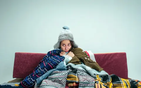 Kobieta w ciąży, otulona wieloma swetrami i kocami, czuje silne uczucie zimna.