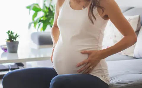 Kobieta w ciąży siedzi na kanapie, dotykając brzucha. Zauważyła brązowe plamienie w ciąży, co ją martwi.