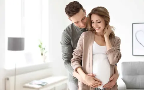 Szczęśliwy mąż obejmuje żonę w ciąży, okazując troskę i miłość. To piękny obraz wsparcia i oczekiwania na dziecko, symbolizujący opiekę na żonę po porodzie.