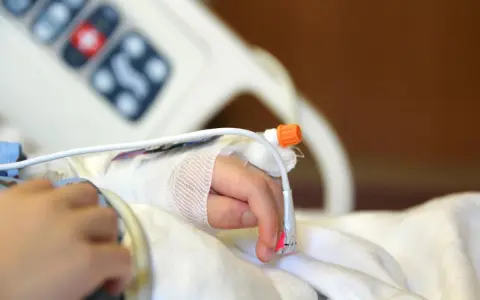 Dziecko z zespołem westa w szpitalu, z wenflonem w dłoni i czujnikiem pulsoksymetru.
