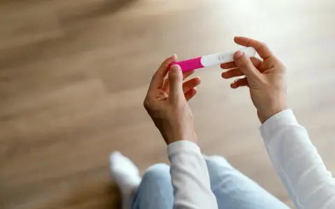Dłonie trzymające test ciążowy, który wskazuje na 1 miesiąc ciąży.