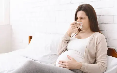 Kobieta w ciąży z chusteczką przy nosie, czuje się niedobrze.
