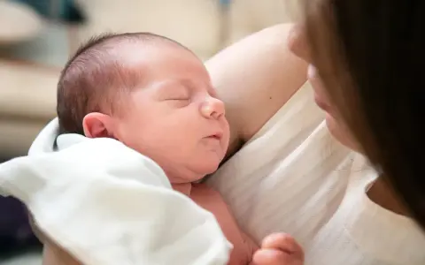 Śpiący noworodek wtulony w ramiona mamy. Delikatne światło podkreśla jego rysy.